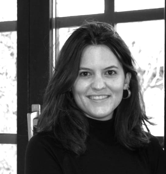 Retrato en blanco y negro de una mujer sonriente con el cabello suelto, frente a una ventana.